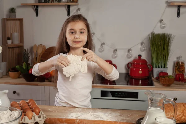 Beyaz bir bluz giymiş güzel küçük kız bir mutfakta bir ekmek pişirme için bir hamur yapıyor.