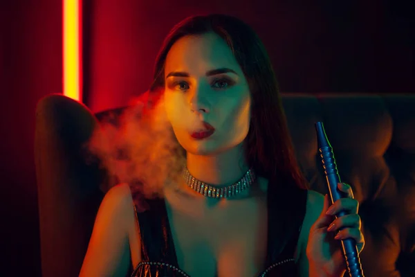 Сексуальная модель брюнетки курит кальян, выдыхая сигарету в роскошном ночном клубе . — стоковое фото