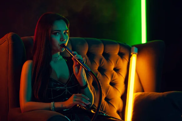 Сексуальная модель брюнетки курит кальян, выдыхая сигарету в роскошном ночном клубе . — стоковое фото