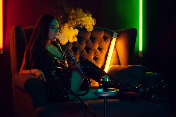 Sexig brunett modell röker en vattenpipa utandning en rök på en lyxig nattklubb. — Stockfoto