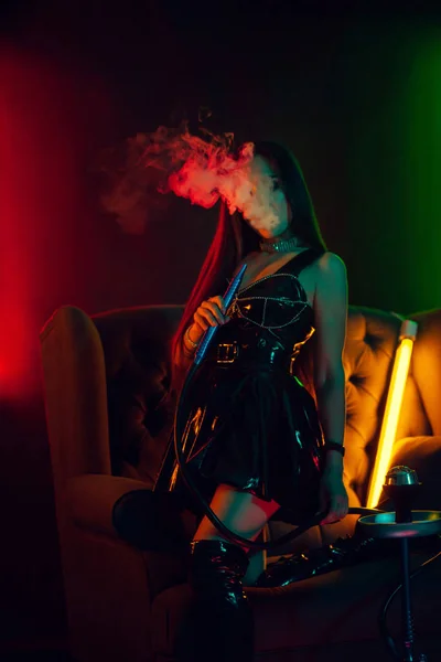 Sexy morena modelo é fumar um narguilé exalando uma fumaça em um clube noturno de luxo . — Fotografia de Stock