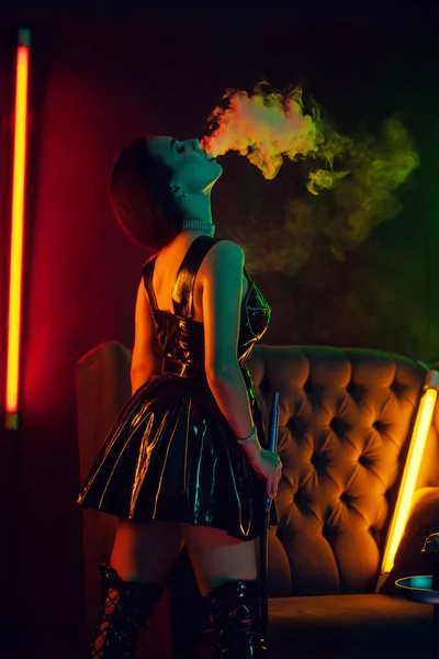 Σέξι μελαχρινή μοντέλο είναι το κάπνισμα ένα χουλέ εκπίοντας ένα κάπνισμα σε ένα πολυτελές νυχτερινό κέντρο. — Φωτογραφία Αρχείου