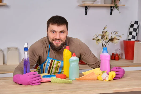 Young handsome bearded man in the kitchen, shows all his cleaning staff - detergents, brushes, sprays. He think he is ready for real cleaning — Stock Photo, Image