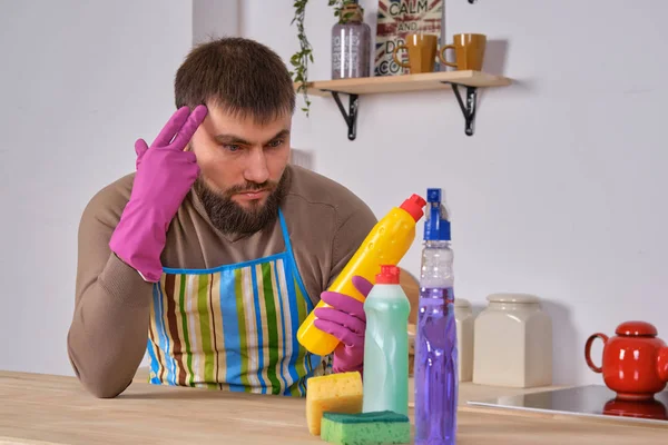 Young man wanted to help his wife in housecleaning, but he doesnt know what to do with all of detergents — Stock Photo, Image