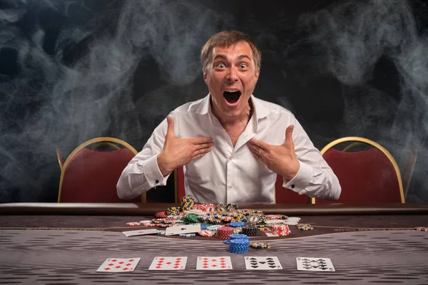 Hombre guapo emocional está jugando póquer sentado en la mesa en el casino . — Foto de Stock