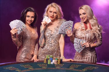 Mükemmel bir saç ve parlak makyaj ile güzel kızlar bir kumar masasında ayakta poz vardır. Casino, poker.
