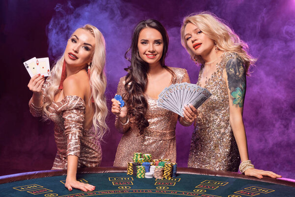 Beautiful girls with a perfect hairstyles and bright make-up are posing standing at a gambling table. Casino, poker.