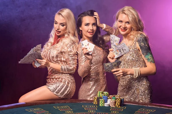 Belle ragazze con un acconciature perfette e trucco luminoso sono in posa in piedi a un tavolo da gioco. Casino, poker . — Foto Stock