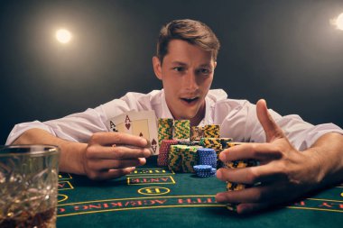 Yakışıklı duygusal adam kumarhanede beyaz spot ışıklarına karşı poker oynuyor..