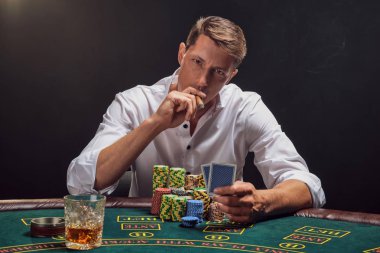 Yakışıklı duygusal adam kumarhanede beyaz spot ışıklarına karşı poker oynuyor..