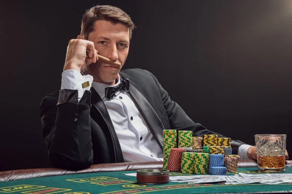 Schöner emotionaler Mann pokert am Tisch im Casino vor weißem Scheinwerferlicht. — Stockfoto