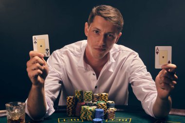 Yakışıklı duygusal adam kumarhanede beyaz spot ışıklarına karşı poker oynuyor..