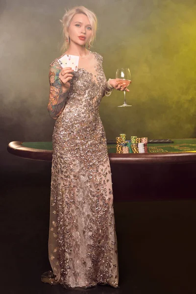 美しい髪型と完璧なメイクアップを持つブロンドの女性は、彼女の手の中に2枚のトランプでポーズをとっています。カジノ, ポーカー. — ストック写真