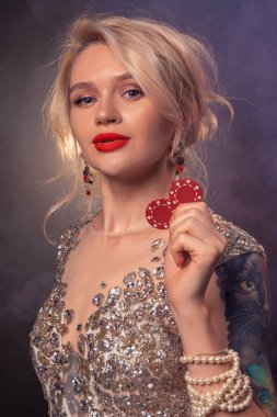 Güzel bir saç modeli ve mükemmel makyaj ile Sarışın kadın elinde kırmızı kumar cips ile poz veriyor. Casino, poker.