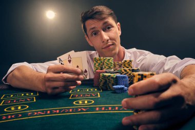 Yakışıklı duygusal adam kumarhanede beyaz spot ışıklarına karşı poker oynuyor..