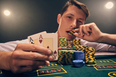 Yakışıklı duygusal adam kumarhanede beyaz spot ışıklarına karşı poker oynuyor..