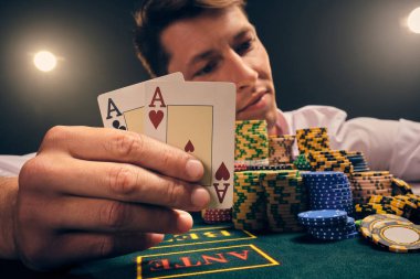 Yakışıklı duygusal adam kumarhanede beyaz spot ışıklarına karşı poker oynuyor..