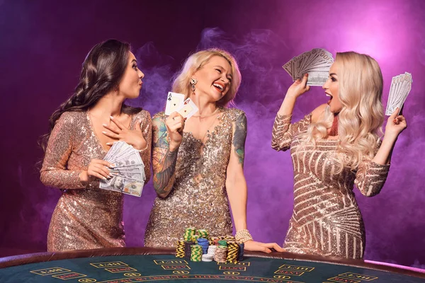 Hermosas chicas con un peinado perfecto y maquillaje brillante están posando de pie en una mesa de juego. Casino, poker . — Foto de Stock