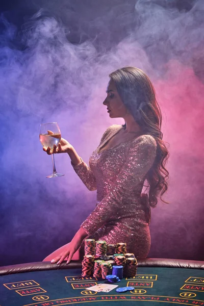 Μελαχρινή κοπέλα με τέλειο χτένισμα και φωτεινό μακιγιάζ ποζάρει με ένα ποτήρι σαμπάνια στο χέρι της. Καζίνο, πόκερ. — Φωτογραφία Αρχείου