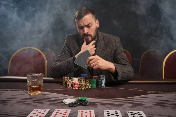Hombre barbudo guapo está jugando póquer sentado en la mesa en el casino . —  Fotos de Stock
