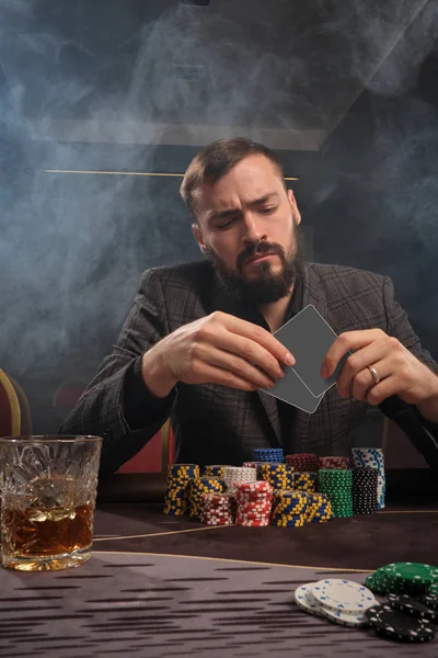 Όμορφος γενειοφόρος άνδρας παίζει πόκερ κάθεται στο τραπέζι στο καζίνο. — Φωτογραφία Αρχείου