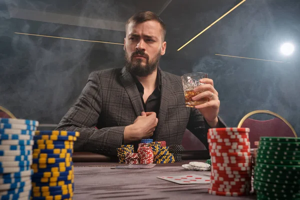 Hombre barbudo guapo está jugando póquer sentado en la mesa en el casino . — Foto de Stock