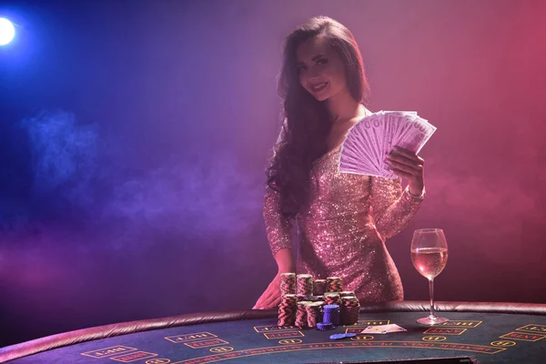 Chica morena con un peinado perfecto y maquillaje brillante está posando con abanico de billetes de cien dólares en sus manos. Casino, poker . — Foto de Stock