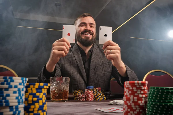 Bonito homem barbudo está jogando poker sentado na mesa no cassino . — Fotografia de Stock