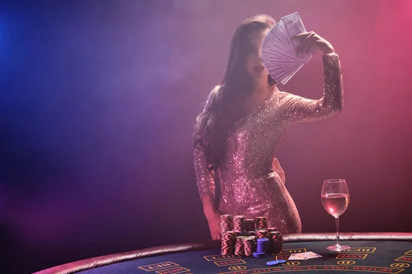 Chica morena con un peinado perfecto y maquillaje brillante está posando con abanico de billetes de cien dólares en sus manos. Casino, poker . —  Fotos de Stock