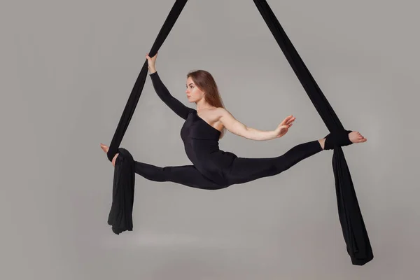 Beautiful girl in a black sport suit is performing an acrobatic elements in a studio.