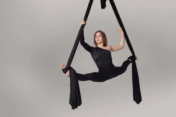 Hermosa chica en un traje deportivo negro está realizando un acrobático elementos en un estudio . — Foto de Stock