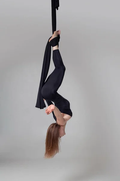 Hermosa chica en un traje deportivo negro está realizando un acrobático elementos en un estudio . — Foto de Stock