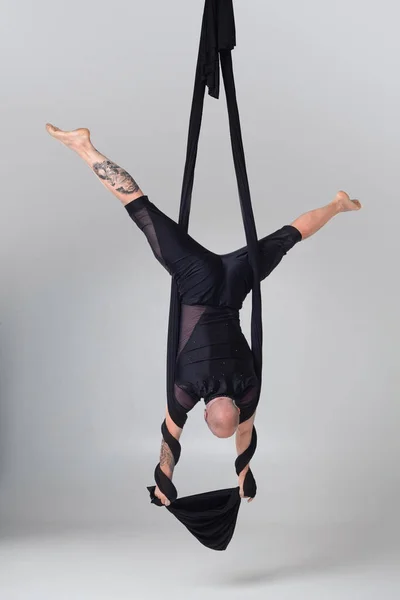 Athletic man in a black sport suit is performing an acrobatic elements in a studio.