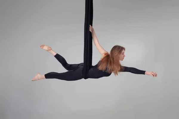 Hermosa chica en un traje deportivo negro está realizando un acrobático elementos en un estudio . — Foto de Stock