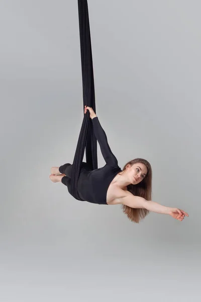 Beautiful girl in a black sport suit is performing an acrobatic elements in a studio.