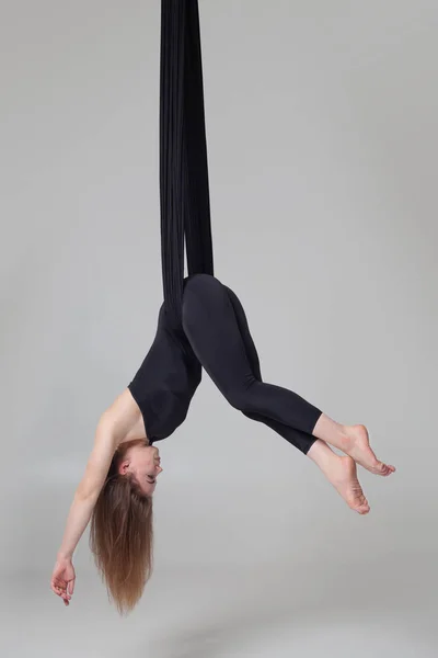 Hermosa chica en un traje deportivo negro está realizando un acrobático elementos en un estudio . — Foto de Stock