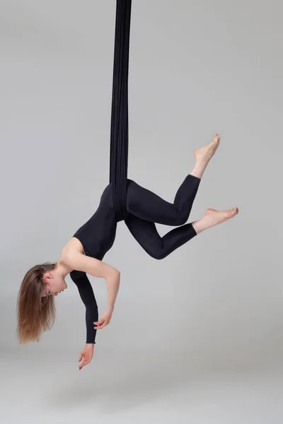 Mooi meisje in een zwart sport pak is het uitvoeren van een acrobatische elementen in een studio. — Stockfoto