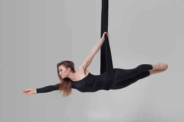 Gyönyörű lány egy fekete sport öltönyt végez akrobatikus elemek egy stúdióban. — Stock Fotó
