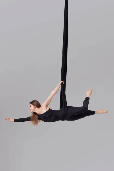 Hermosa chica en un traje deportivo negro está realizando un acrobático elementos en un estudio . — Foto de Stock