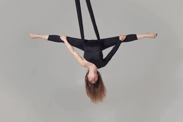 Mooi meisje in een zwart sport pak is het uitvoeren van een acrobatische elementen in een studio. — Stockfoto