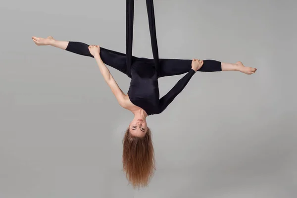 Mooi meisje in een zwart sport pak is het uitvoeren van een acrobatische elementen in een studio. — Stockfoto