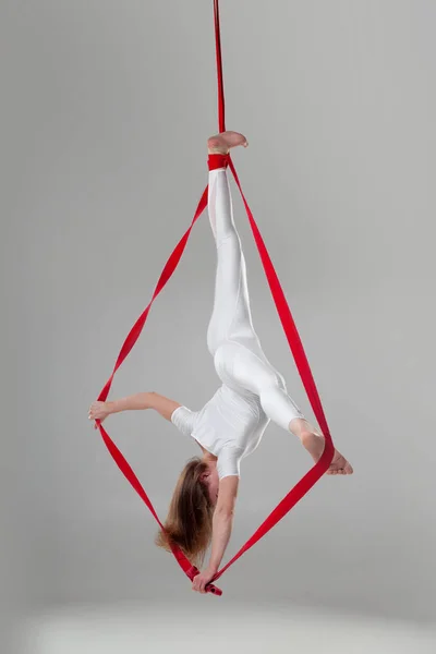 Mooi meisje in een wit sport pak is het uitvoeren van een acrobatische elementen in een studio. — Stockfoto