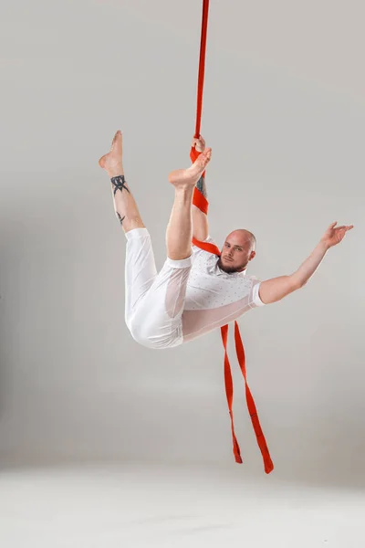 Atletische man in een witte sport pak is het uitvoeren van een acrobatische elementen in een studio. — Stockfoto