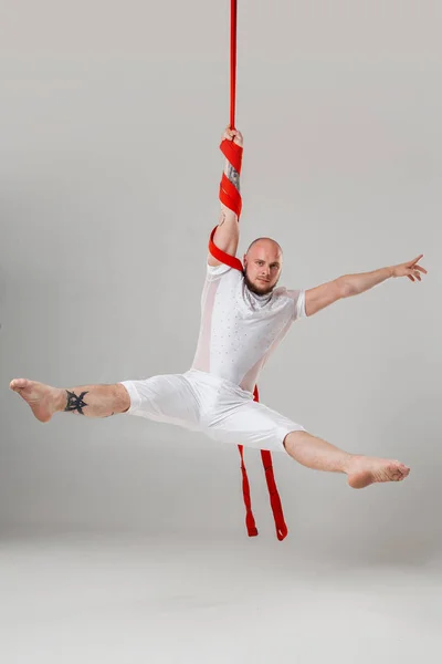 Atletische man in een witte sport pak is het uitvoeren van een acrobatische elementen in een studio. — Stockfoto