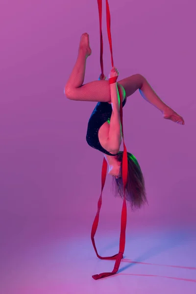 Beautiful girl in a black swimsuit is performing an acrobatic elements in studio.