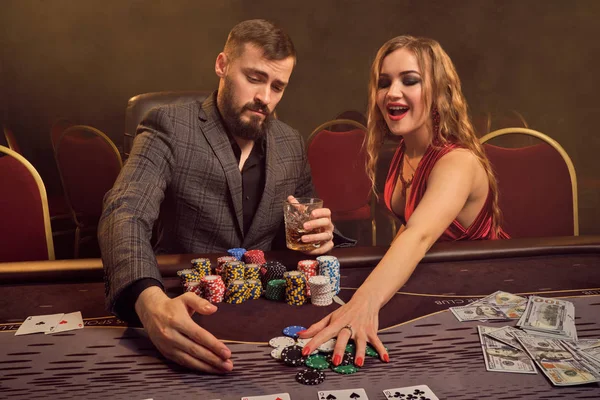 Charming wealthy couple are playing poker at a casino.