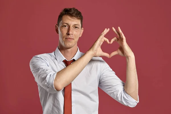 Jongeman in een klassiek wit shirt en rode stropdas poserend over een roze achtergrond. — Stockfoto