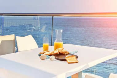 İki kişilik masa, açık hava otel balkonunda deniz manzaralı bir kahvaltıyla servis edilecek..