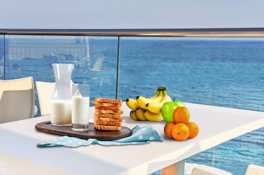 İki kişilik masa, açık hava otel balkonunda deniz manzaralı bir kahvaltıyla servis edilecek..