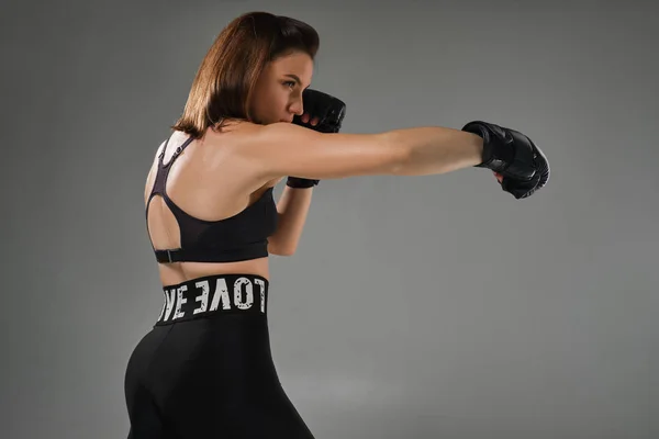 Mulher atlética em luvas de boxe está praticando karatê em estúdio . — Fotografia de Stock